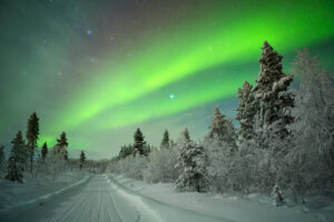 Aurora borealis over a road through winter landscape in Finnish Lapland